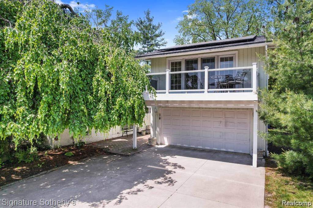 View of front facade with solar panels, a balcony, driveway, and an attached garage at 2372 Pine Lake Road, West Bloomfield, MI 48324